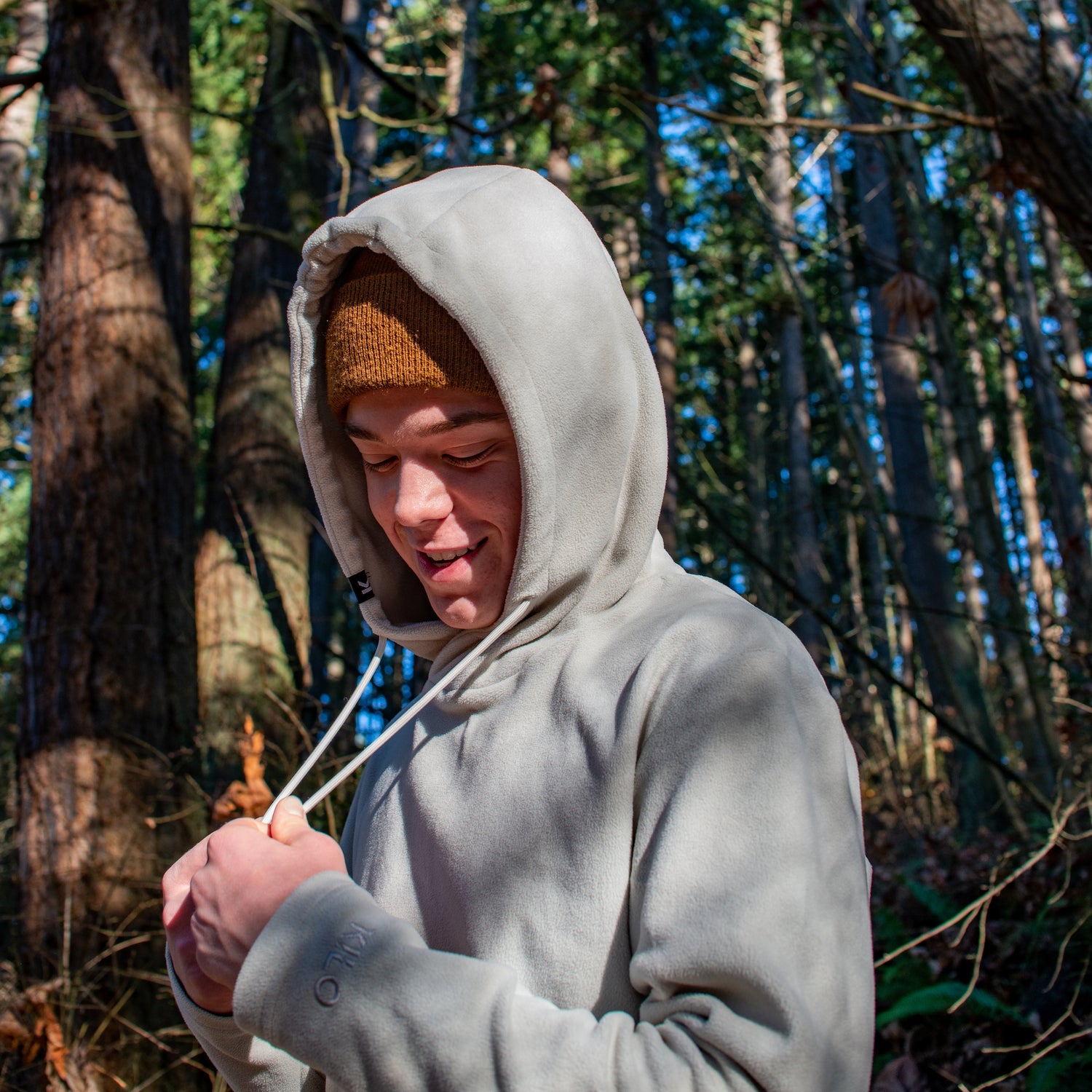 Grey Sustainable polar fleece hoodie made from recycled fabric. Unisex Athletic fit, moisture wicking, lightweight, cozy and comfortable. Perfect for the outdoors or working from home. Grey hoodie in the forest in the Pacific North West.